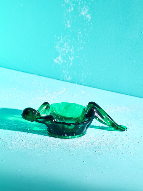 A hunter green bathing lady dish on a turquoise background.