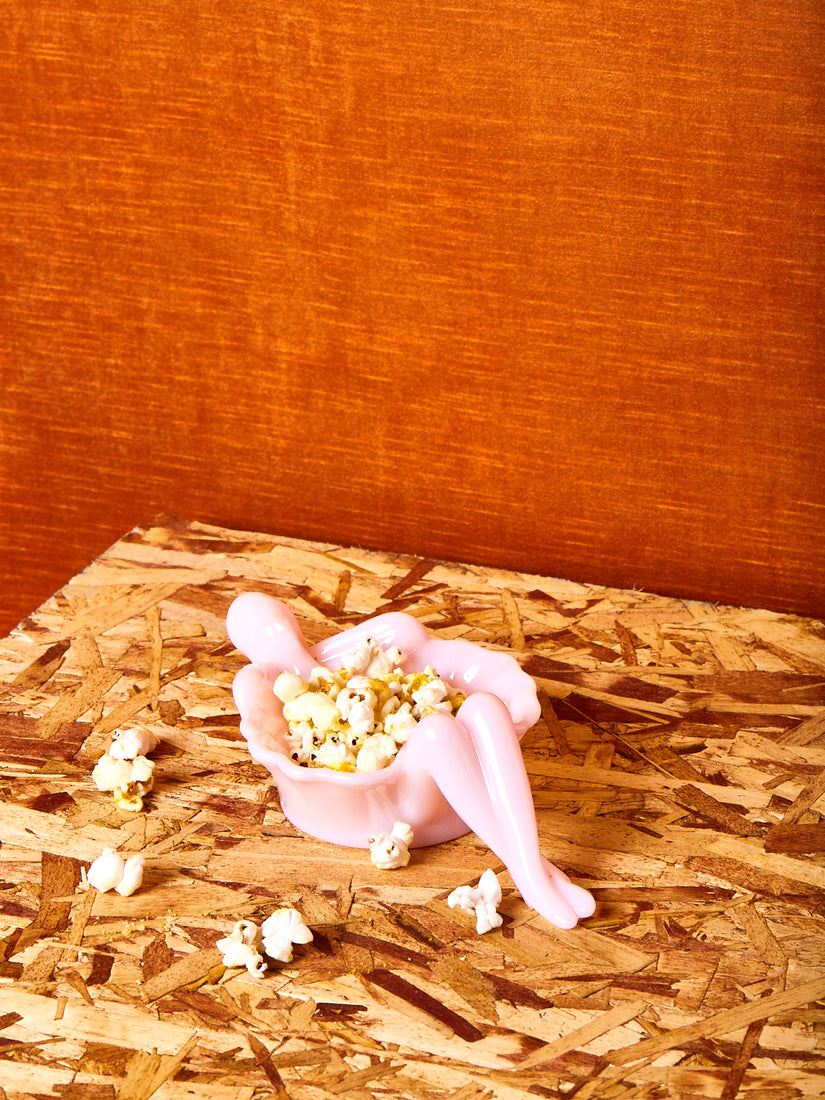 A milk pink bathing lady with popcorn inside and scattered around wooden table.