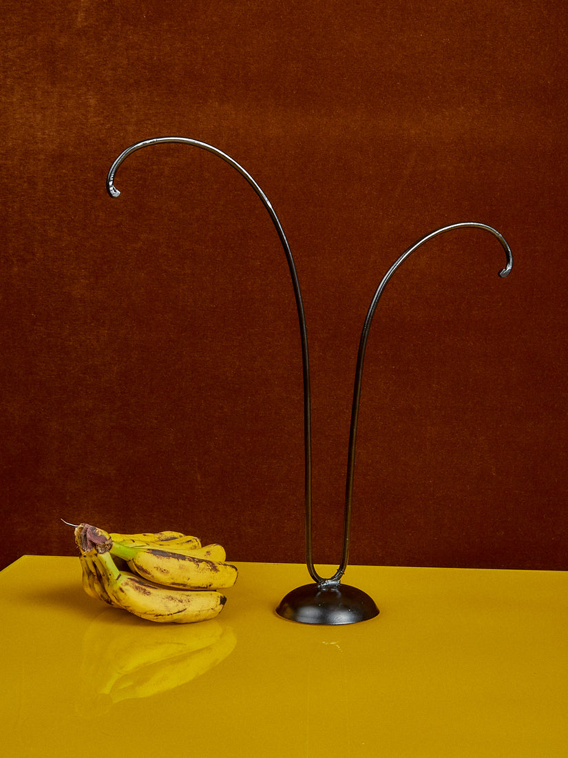 A Banana Tree by Gohar World rests on a yellow surface next to a bunch of ripe baby bananas.