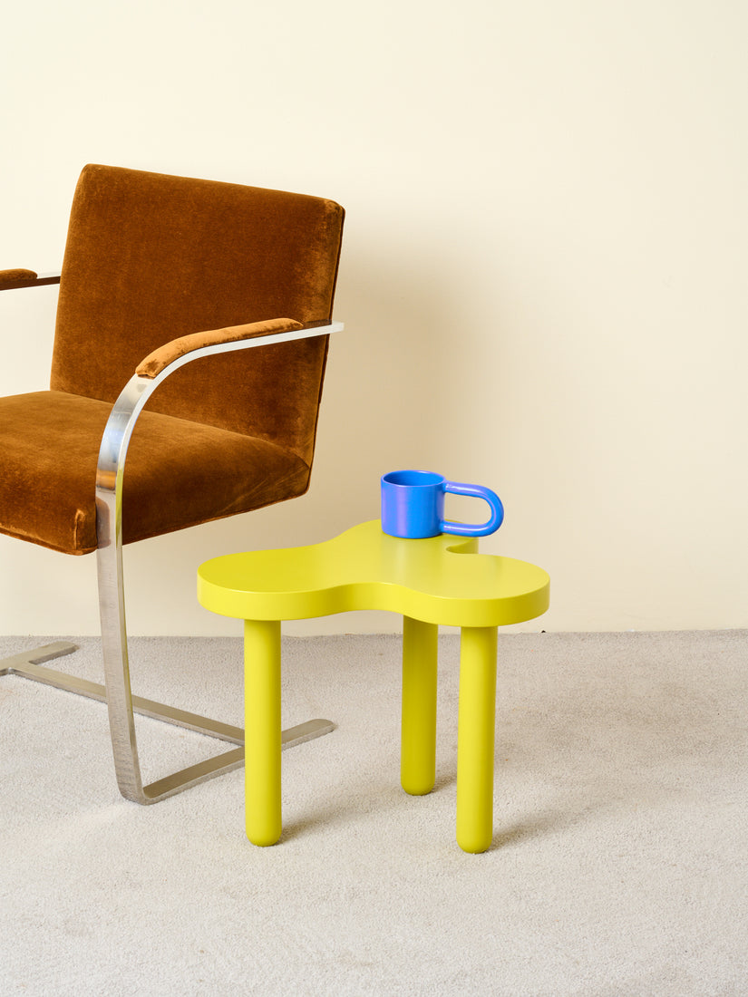 Tall Chartreuse Splat Table sits with a blue stoneware mug atop, next to a brown Brno Chair by Mies van der Rohe.