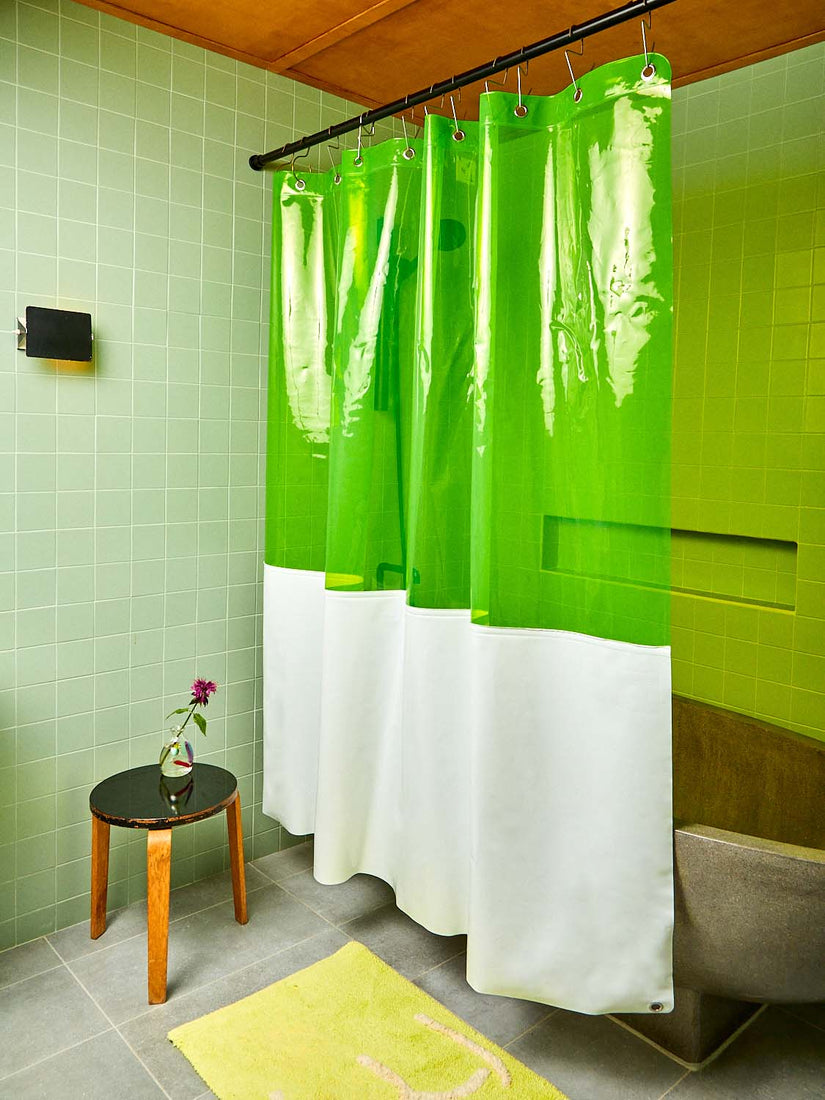 The Zinc Sun Shower Curtain hanging in front of a stone tub, in a sage green tiled bathroom.