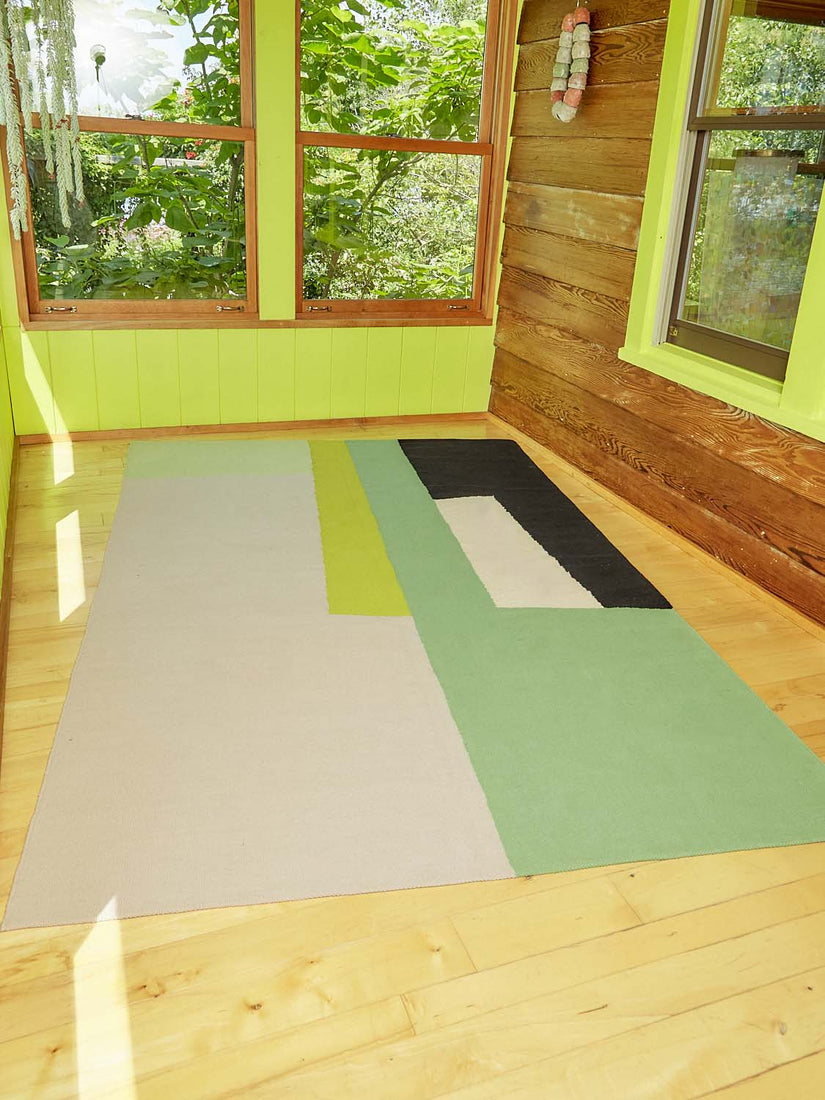 The Earthworm Rug by Cold Picnic featuring beige, green, lime gree, cream, and black abstract pattern.