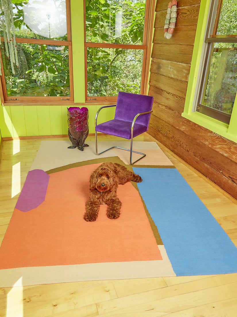 A woven rug by Cold Picnic with a purple velvet and chrome chair atop. A ruby red handmade resin vase and a large tan Golden-doodle dog sit next to the chair in this lime green room.