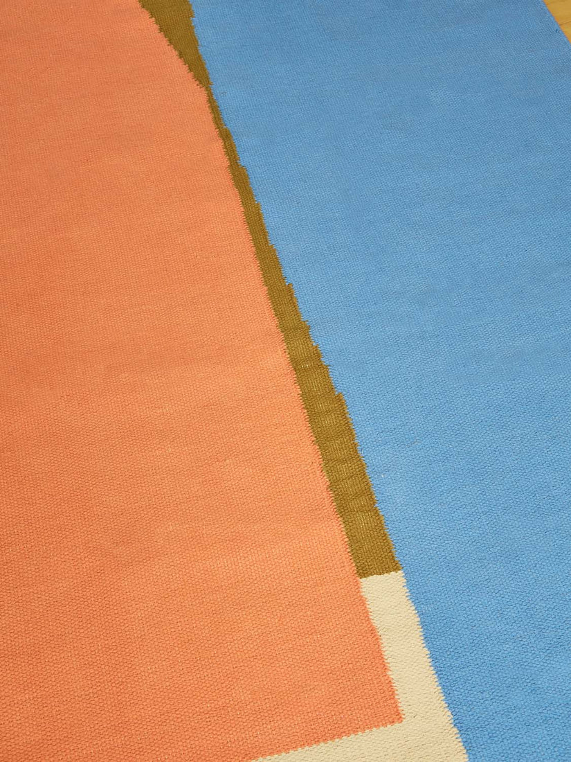 A close up picture of the woven rug by Cold Picnic with the colors orange, blue,  and magenta showing.
