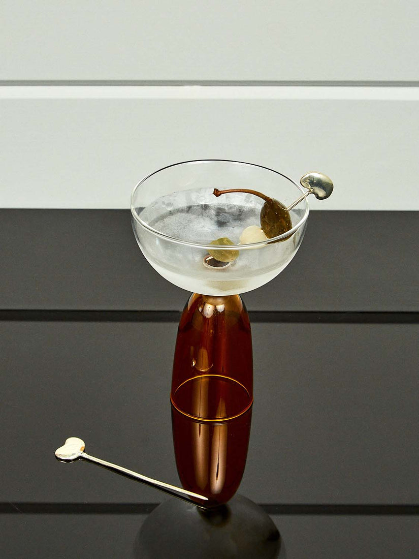 A Bean Toothpick holds an olive, onion, and pepper inside a MaMo Coo Coupe with a martini. Another toothpick rests beside the glass.