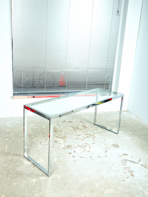 The vintage chrome and glass console sits in a room on a slight angle. The room has the shades pulled down and the floor is concrete.