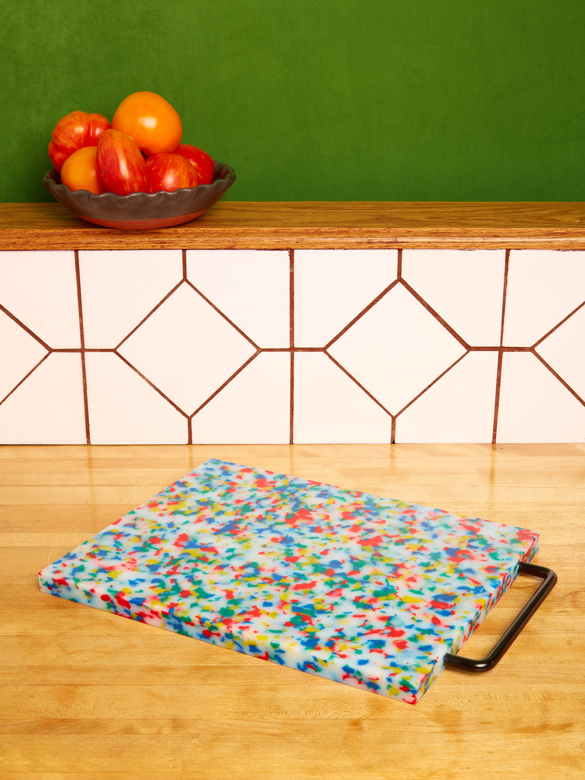 A plastic chopping block with a multicolored and white pattern, featuring a metal handle.