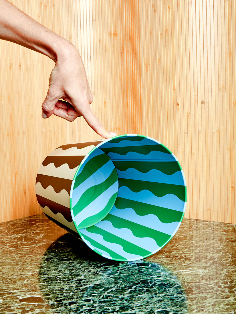 The black and white river pattern bin lays on its side with a hand pressing it in place by a single finger.