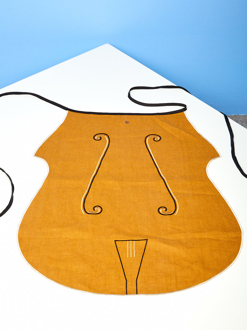 Brown linen Cello Apron by Maison Blazac. Cut in the shape of a cello with embroidery detailing the components of a cello.