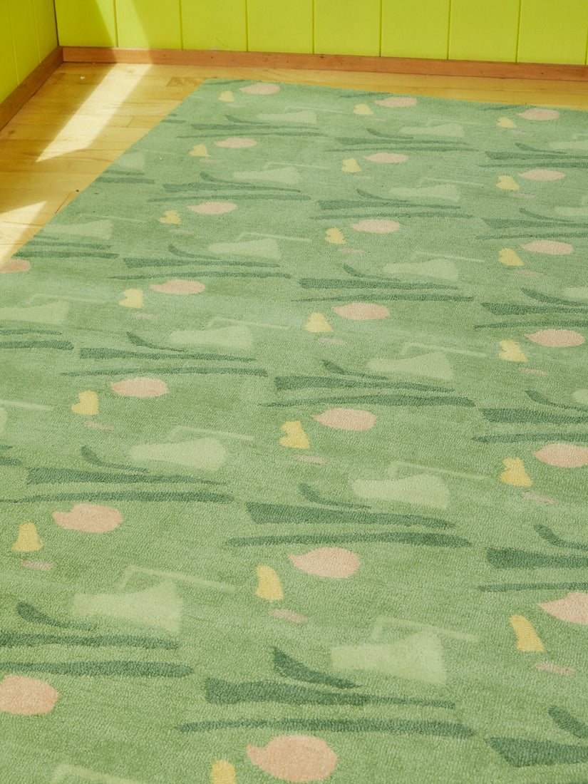 Mostly green rug with an abstract pattern of lighter green, darker green, peach, and pale yellow.