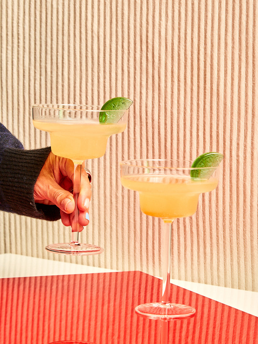 Two margaritas in Maison Balzac Margarita glasses. A hand holds one of the glasses up.