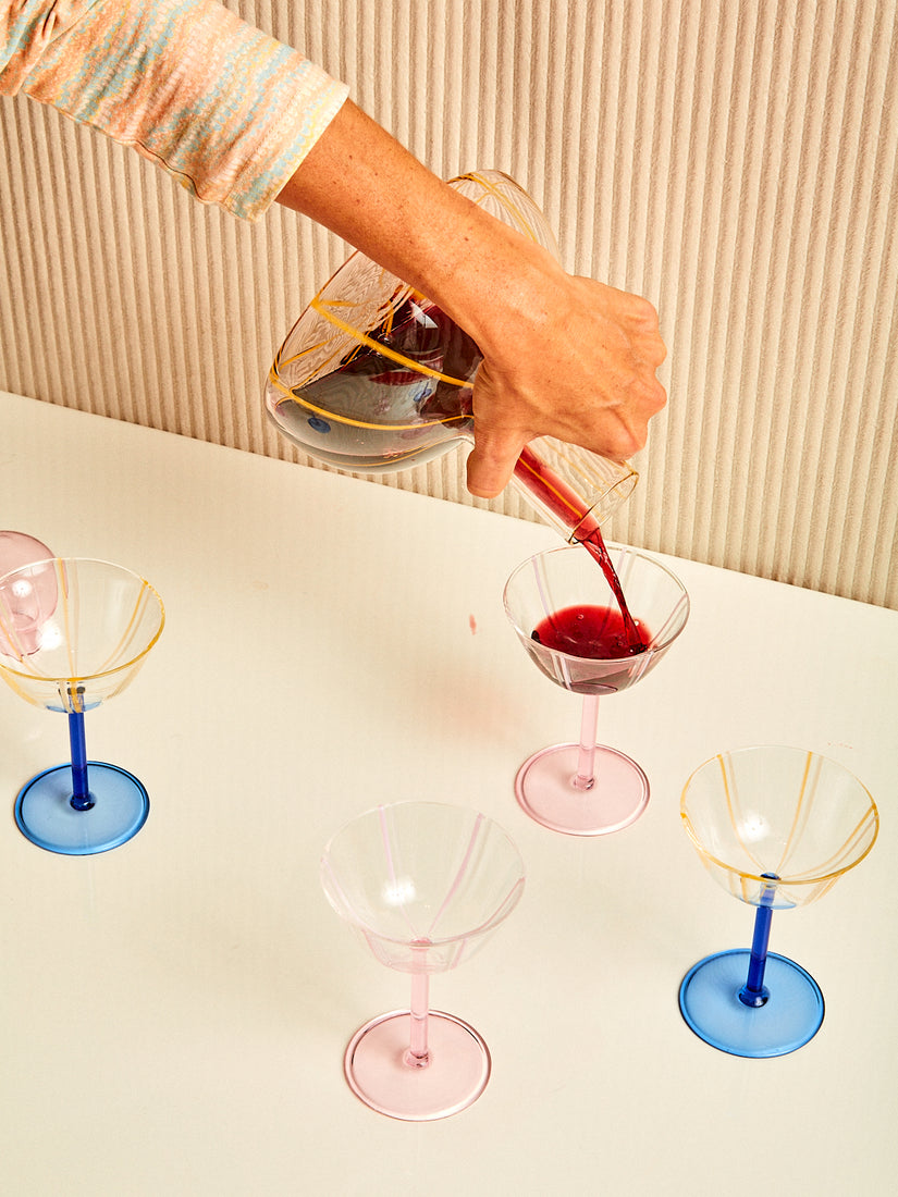 A hand pours of glass of red wine from the Grand Soleil Decanter into a coupe.