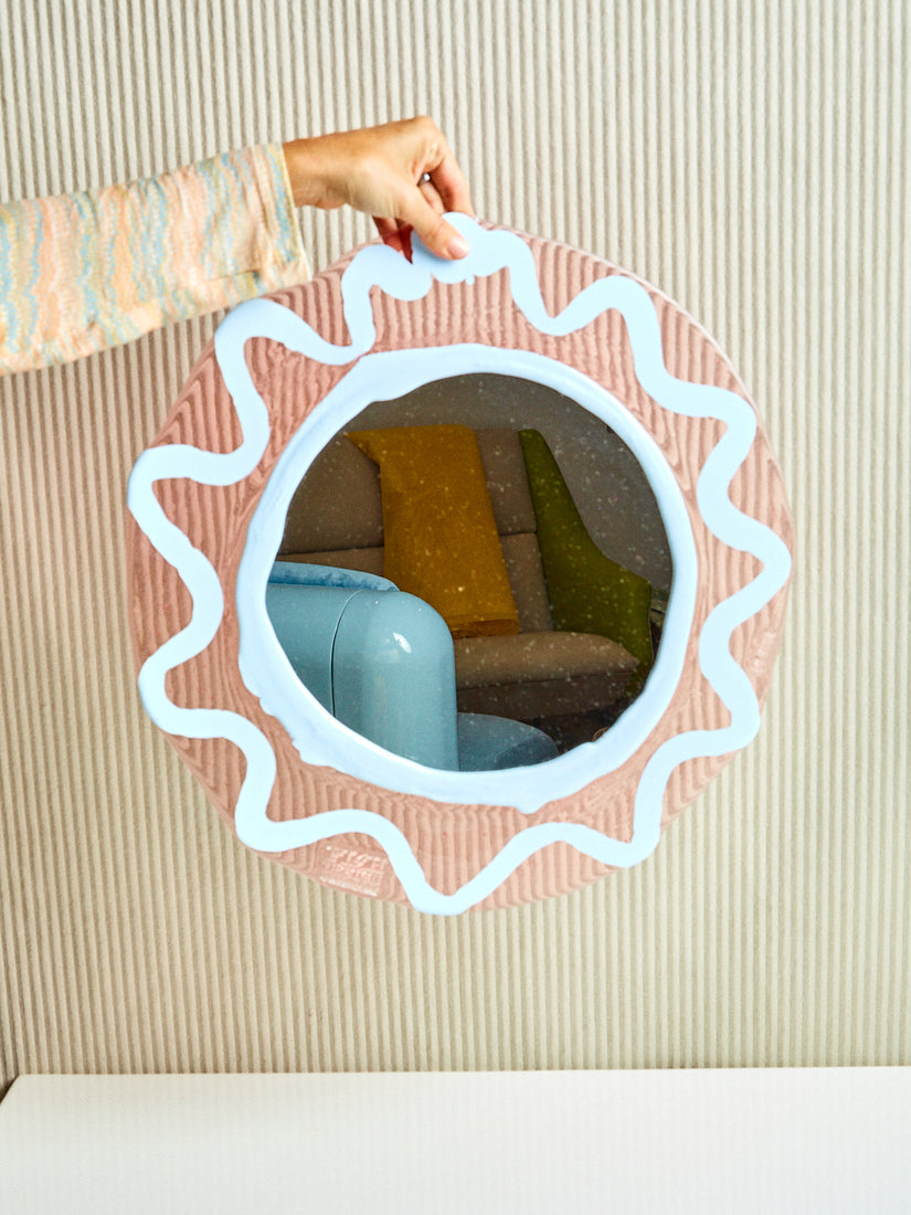 A hand holds up the Round Mirror in Peach and Blue by Gaetano Pesce for Fish Design.