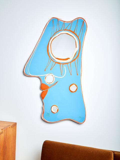 A sky blue face shaped mirror with orange and pale pink accents.