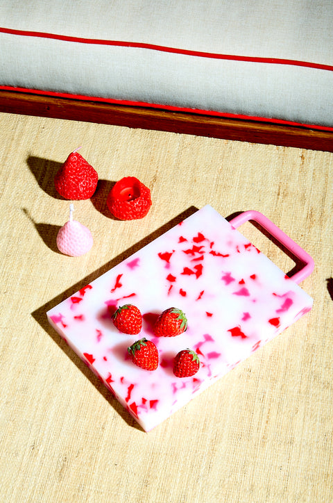 A white and pink small chopping block with strawberries.