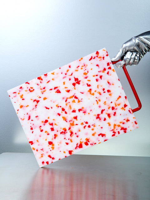 A multicolored plastic chopping block with a red metal handle, displayed on a metal surface.