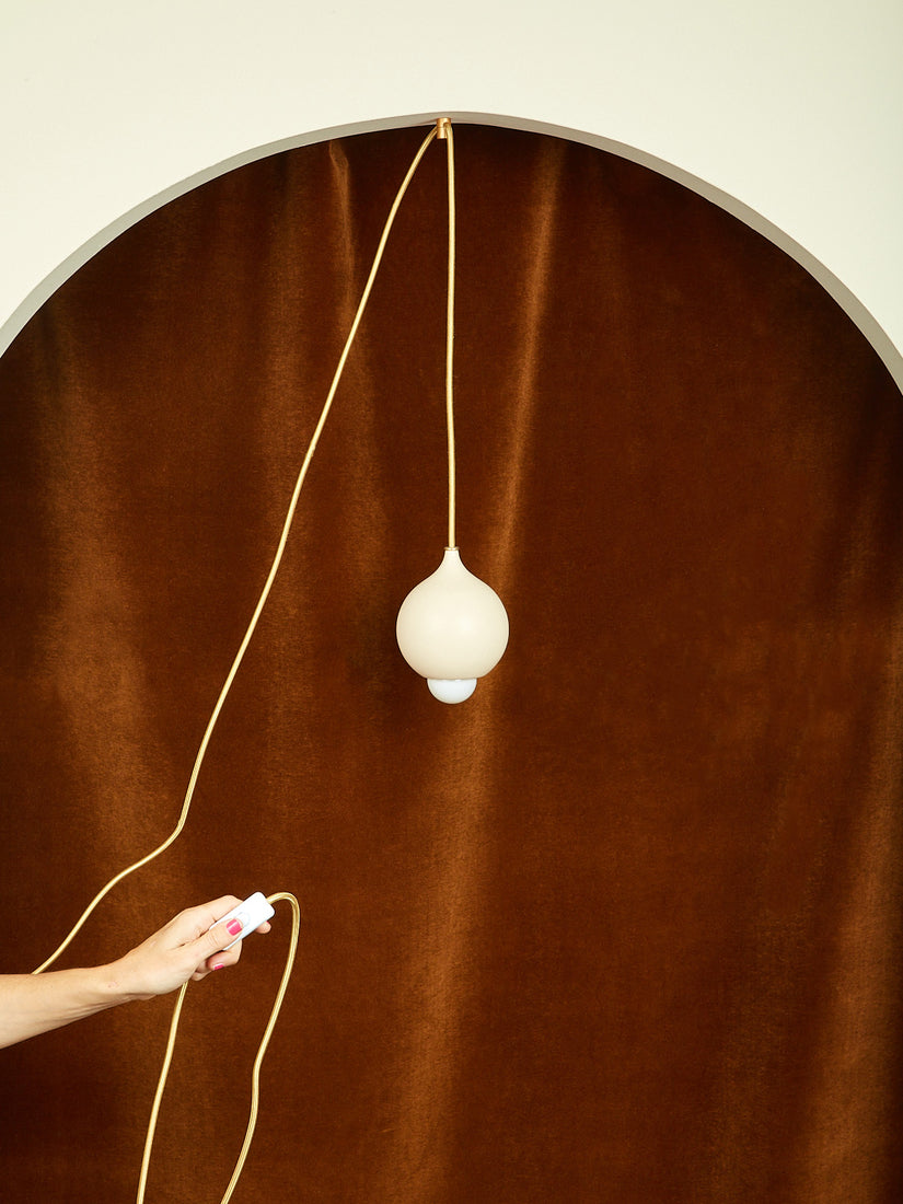 A hand holding up the switch-on-cord of a matte cream Droplet Pendant by Entler.