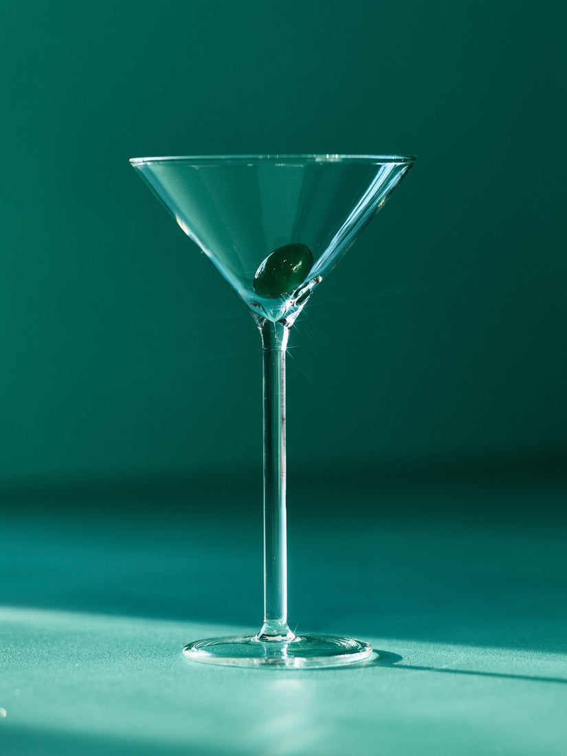 A clear martini glass with a glass olive inside the glass.