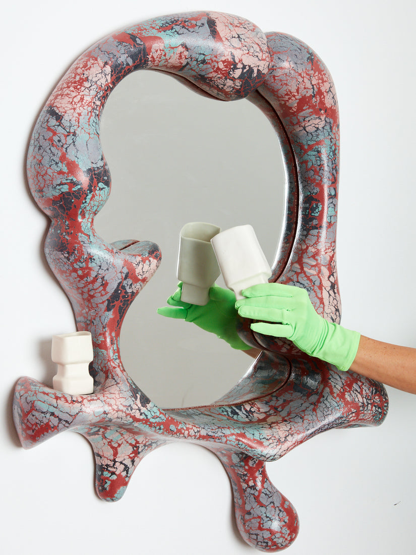 A hand holds a ceramic cup in front of the iris mirror while another cup rests on the mirror.