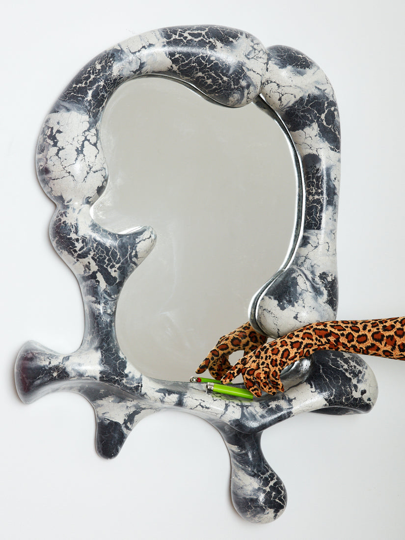 A hand wearing a leopard print glove reached for a green lighter resting on the ledge of a Concrete Cat Iris Mirror.