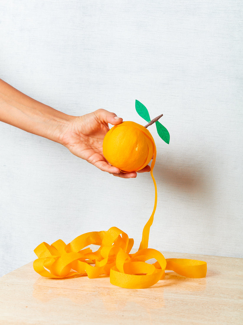 A hand holds up a partially unraveled Orange Surprise Ball by Tops Malibu.