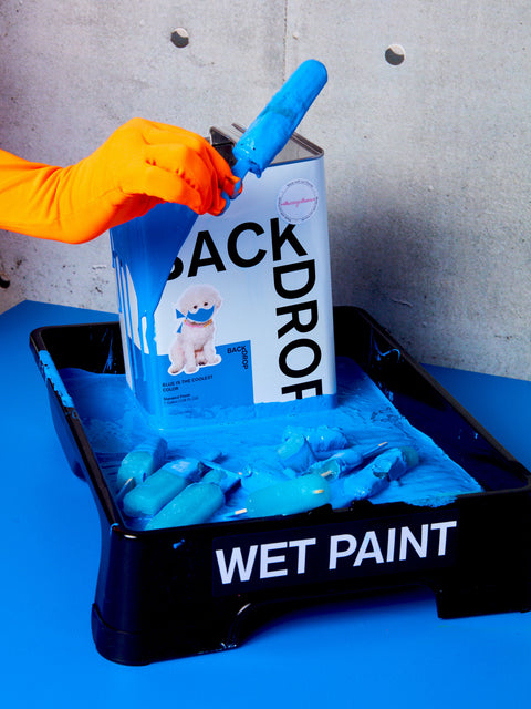 An orange gloved hand holds a blue lollipop in front of "Blue is the Coolest Color" blue paint.
