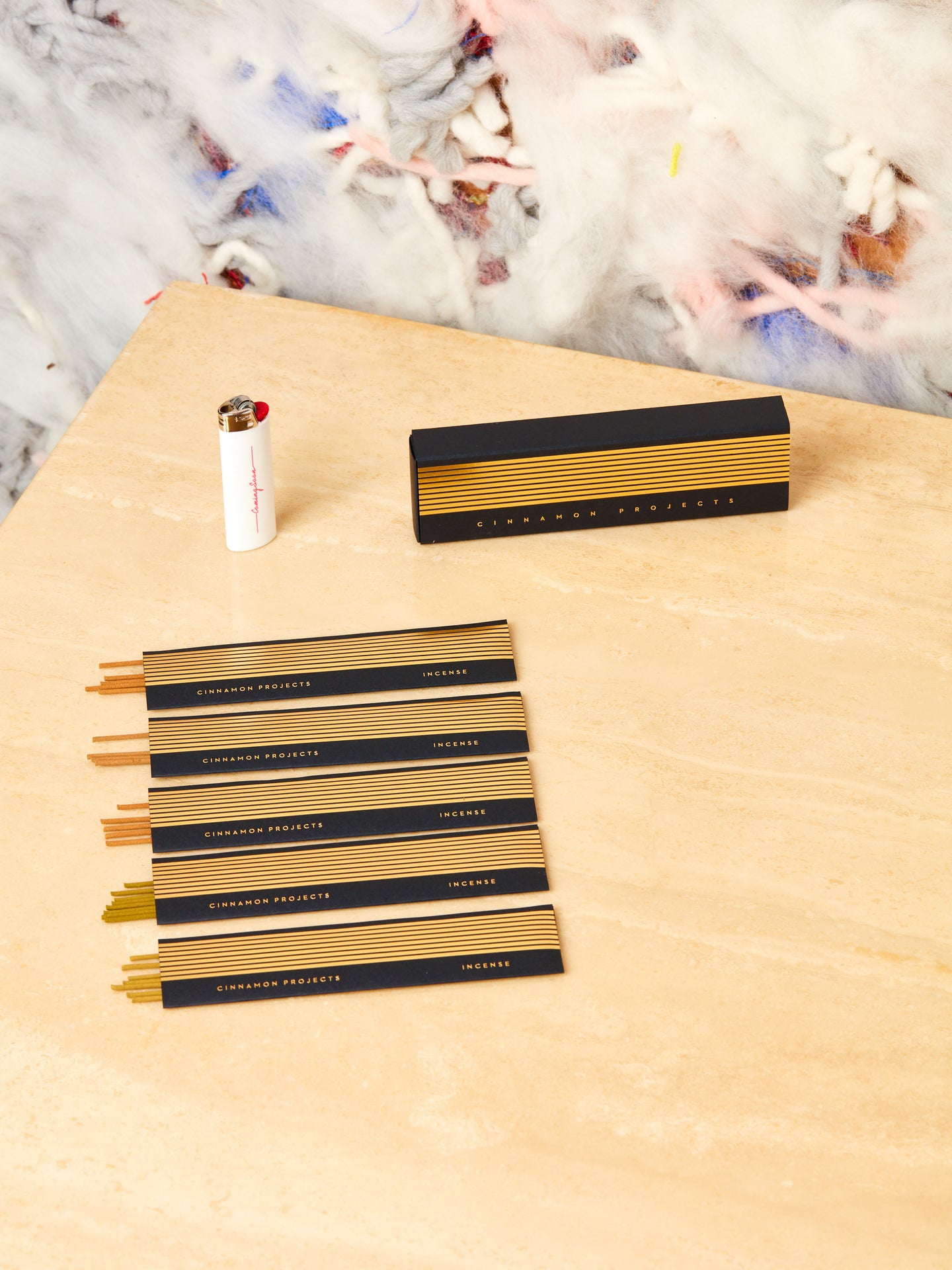 Cinnamon Projects variety pack of incense neatly laid out on display next to a white lighter on a travertine table top.