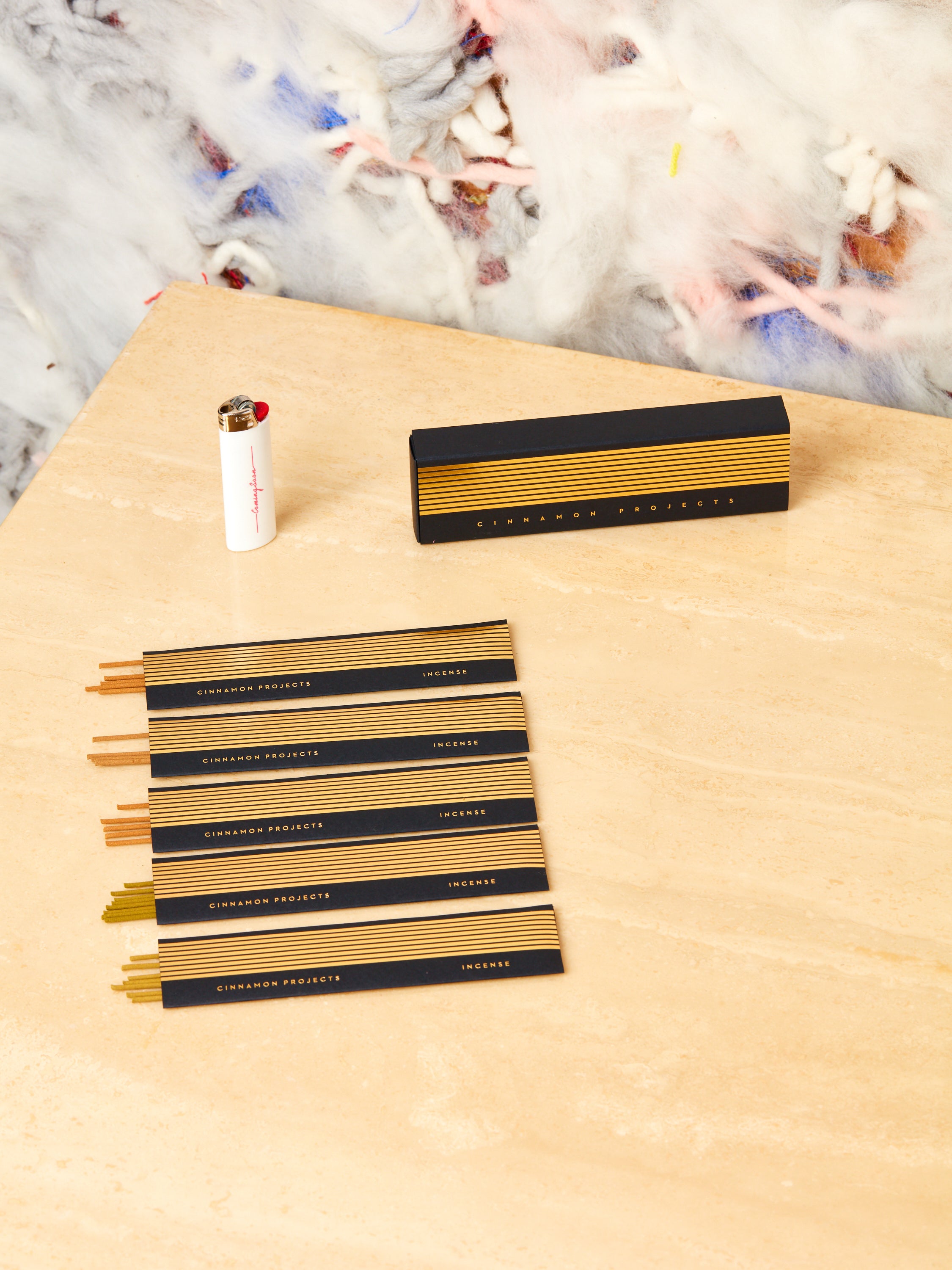 Cinnamon Projects variety pack of incense neatly laid out on display next to a white lighter on a travertine table top.