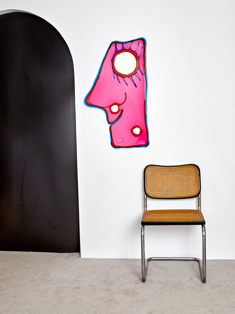 Handmade resin mirror that's mostly transparent pink with 3 round mirros that make up an abstract face, outlined in opaque blue and red resins.