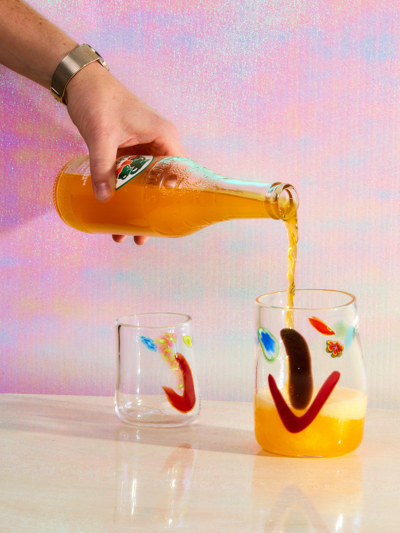 A mandarin jarito's being poured into a tall face vessel glass with a smaller glass sitting next to it.