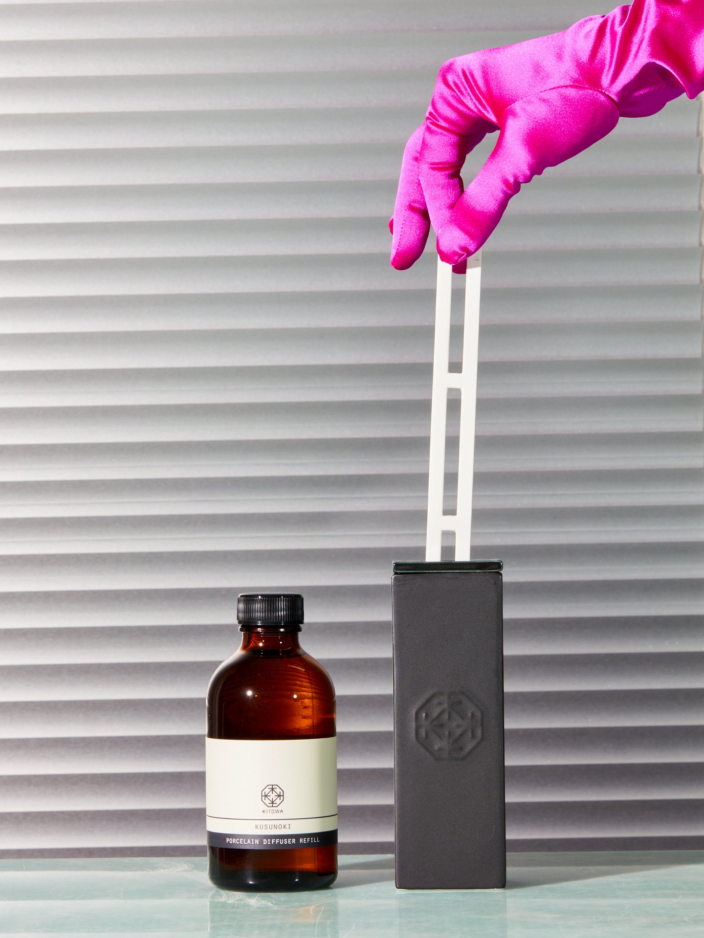 A pink satin gloved hand pinches the porcelain reed of the Kitowa diffuser.