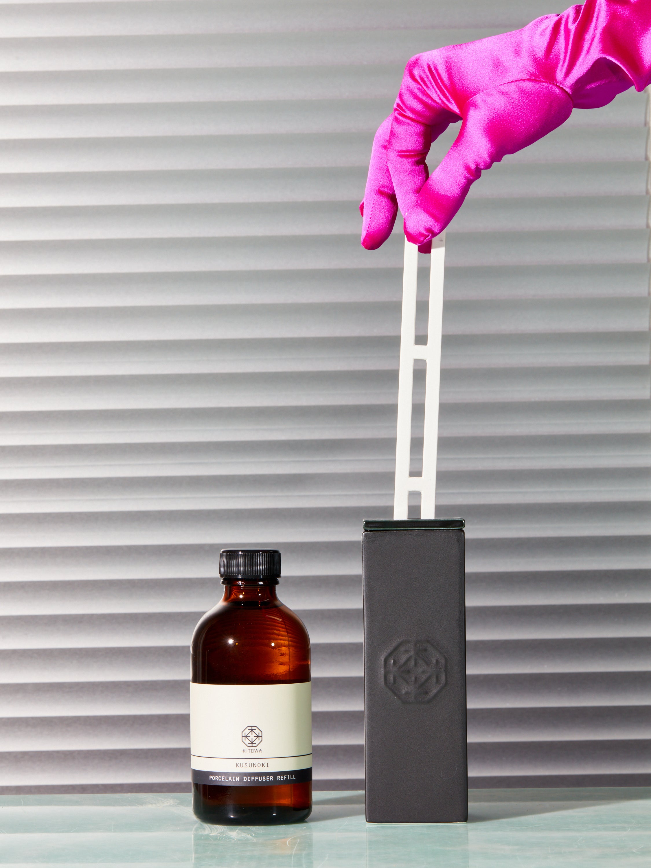 A pink satin gloved hand pinches the porcelain reed of the Kitowa diffuser.