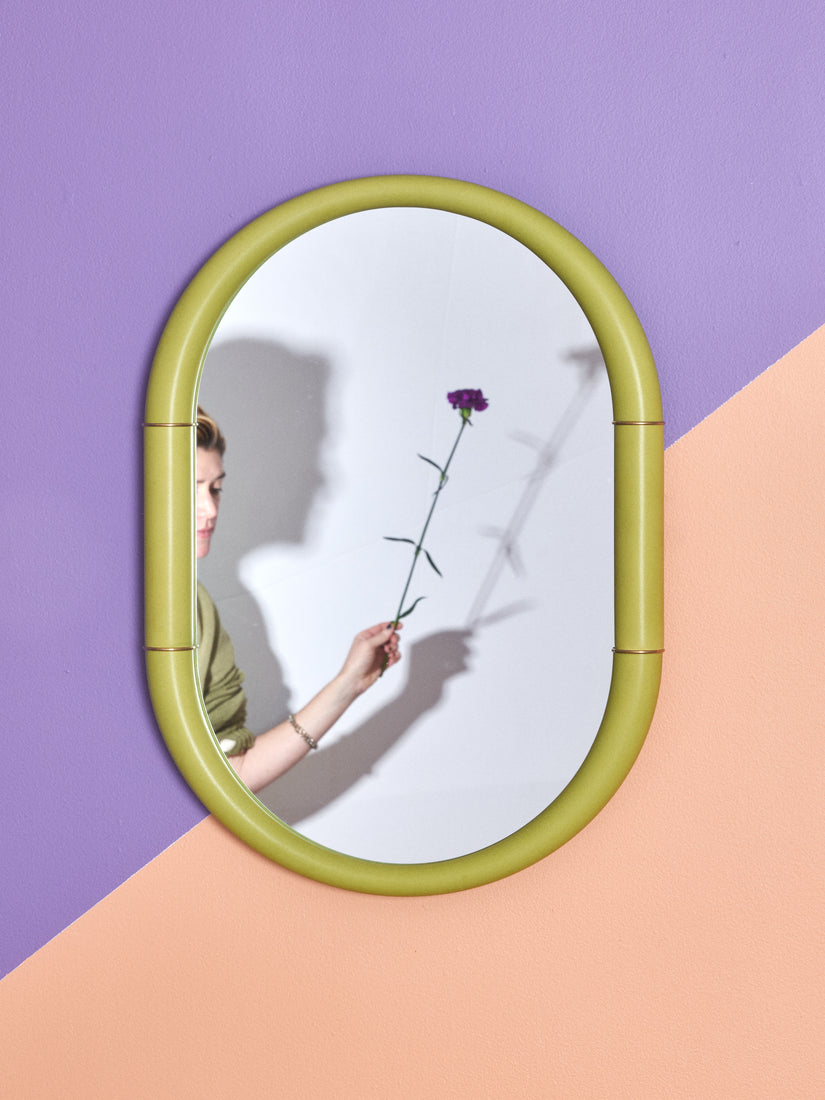 Someone holding a flower can be seen in the reflection of a green Ceramic Mirror by Entler.
