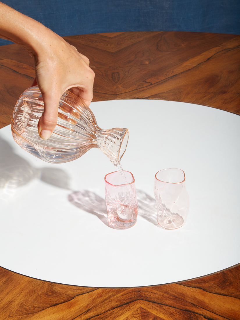 A pink sake carafe pouring into two sake glasses.