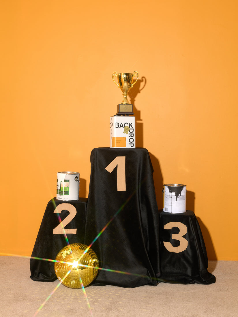 1st, 2nd, and 3rd place podiums with a gold disco ball in front. In first place sits the Color of the Year paint can, atop the can is a trophy.
