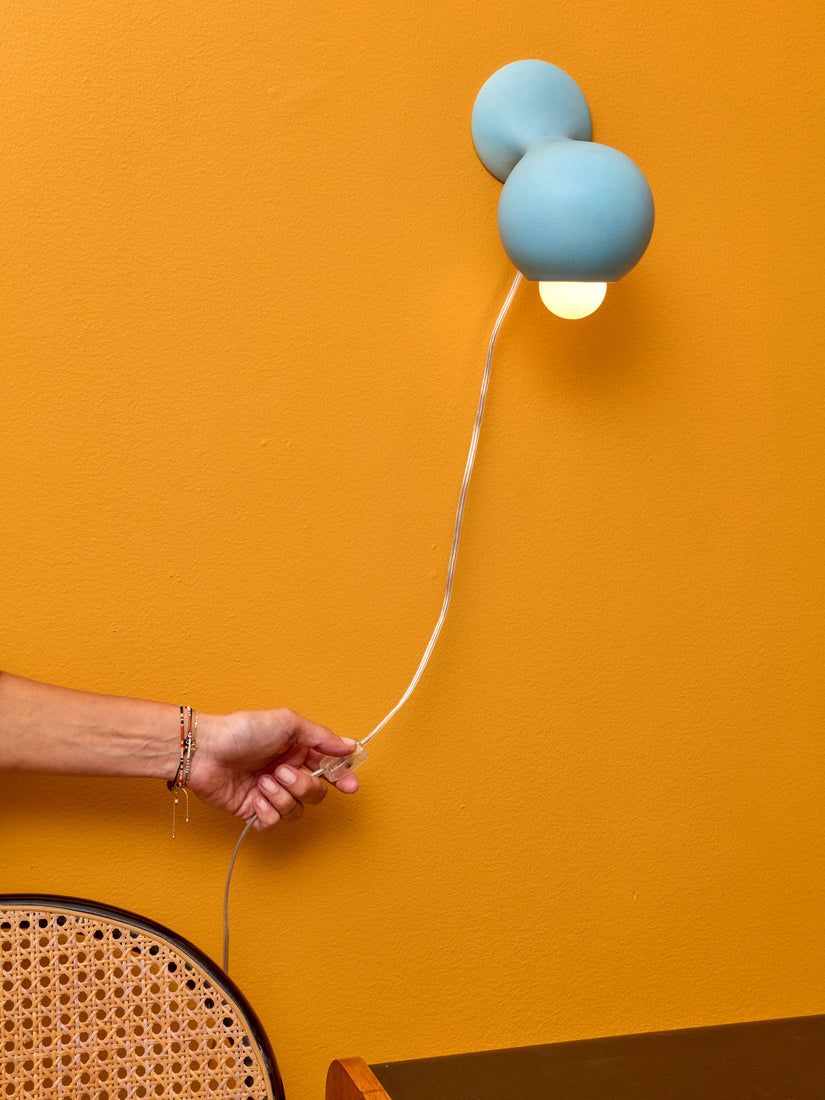 A hand switches on the cord of a blue Little Sconce by Entler.