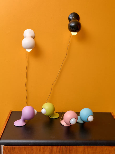 Six Little Sconces by Entler in different colors. The white and black sconces are mounted to a marigold wall while the rest sit atop a dresser.