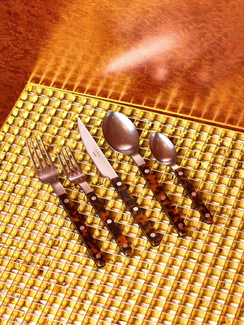 One place setting of Sabre's tortoise bistro flatware against a brass grid surface.