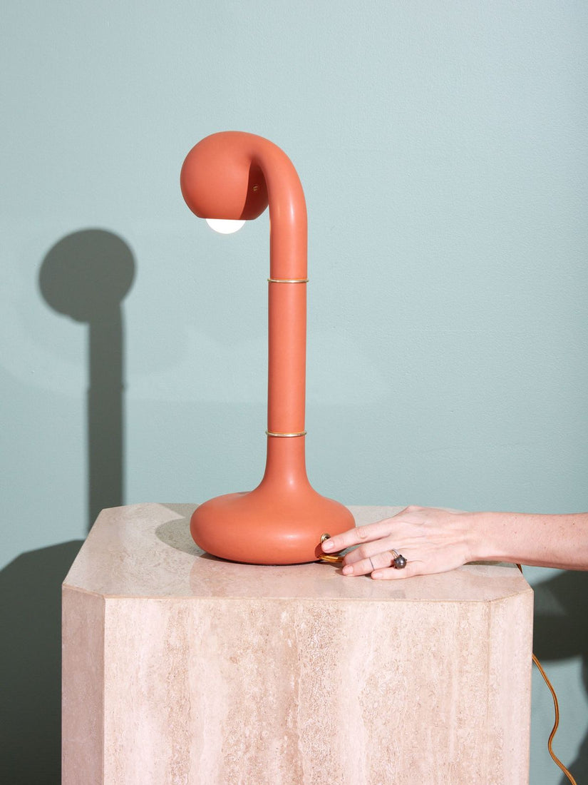 Burnt Orange Ceramic Table Lamp by Entler Studio on a travertine side table. A hand pressing the switch of the lamp.
