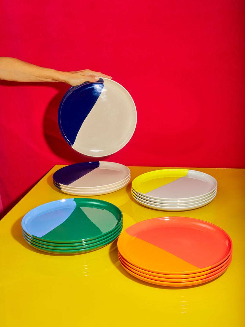 Four sets of 4 Melamine Plates by Thomas Fuchs in different colorways. A hand holds up the top plate from the stack of Ivory Navy Blue plates.