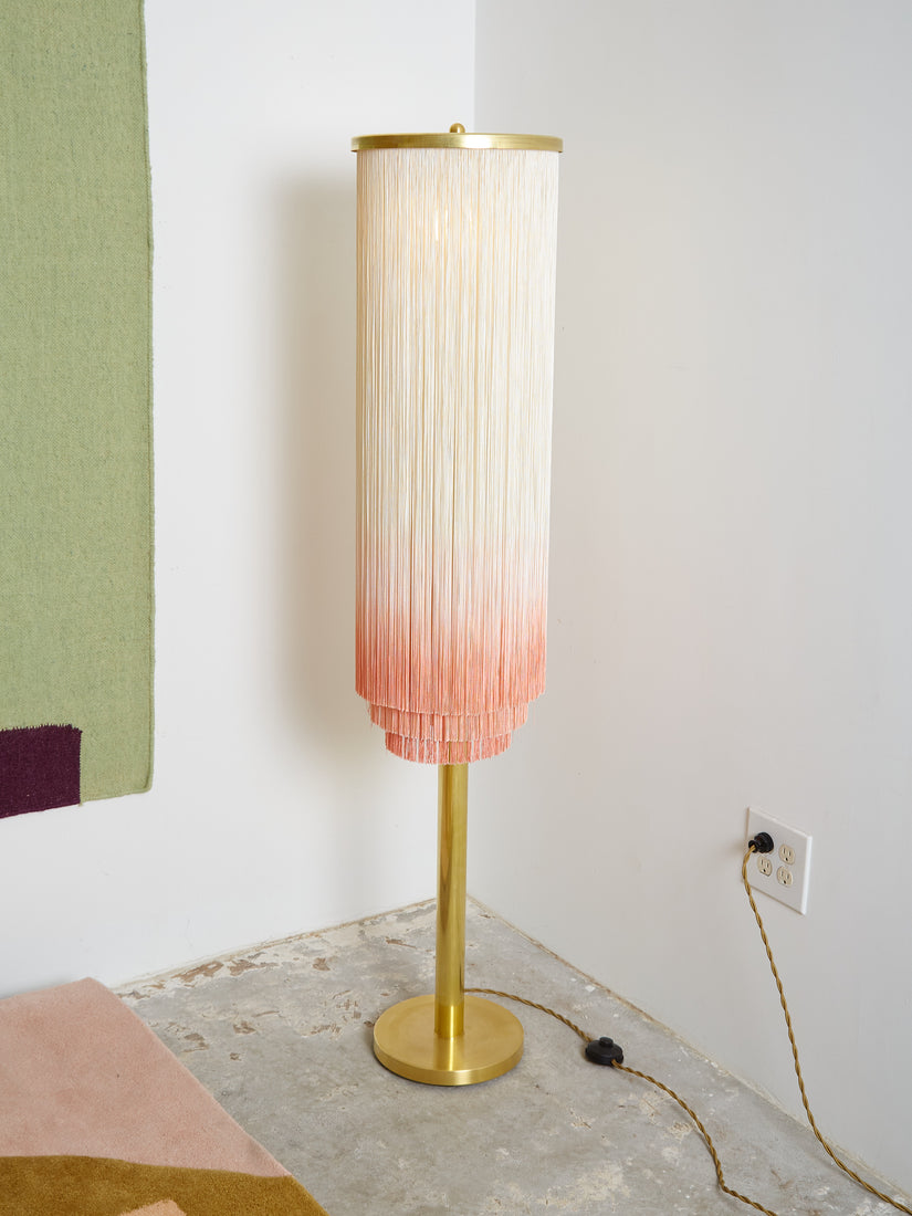 Brass lamp with an exaggerated cream to pink ombre fringe shade.