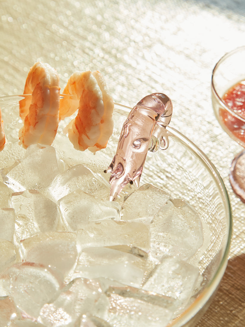 Two shrimps sit on the lip of a Shrimp Cocktail Platter full of ice.