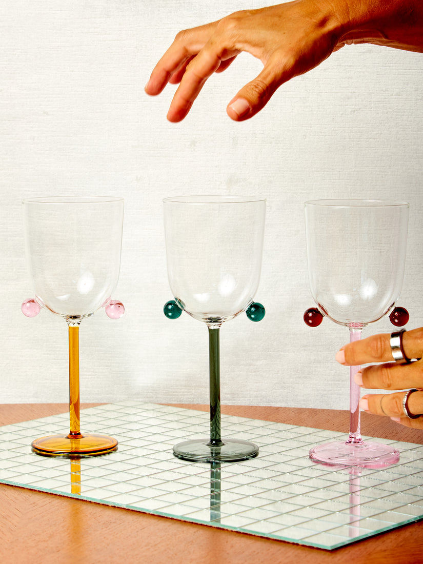 One hand hovers and one hand grabs Pompom Wine Glasses by Maison Balzac.