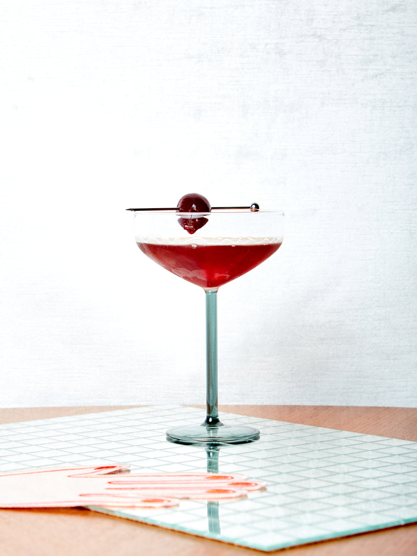 A Manhattan Glass with a Manhattan poured inside and skewered cherry atop.