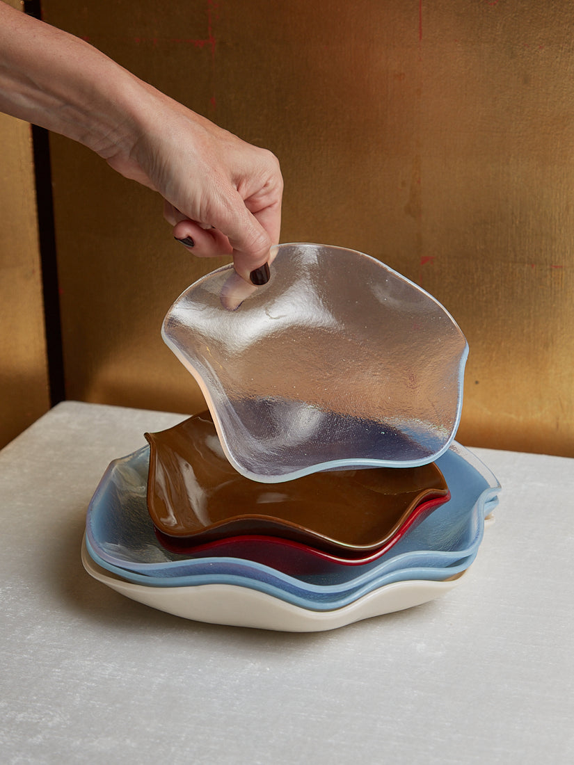A stack of 6 Petal Plates by Sophie Lou Jacobsen. A hand holds up the top small opal plate.