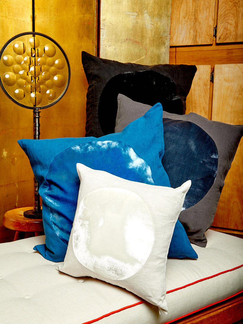 A black, charcoal, blue, and ivory Velvet Circle Pillow by Correll Correll piled up on a white daybed.