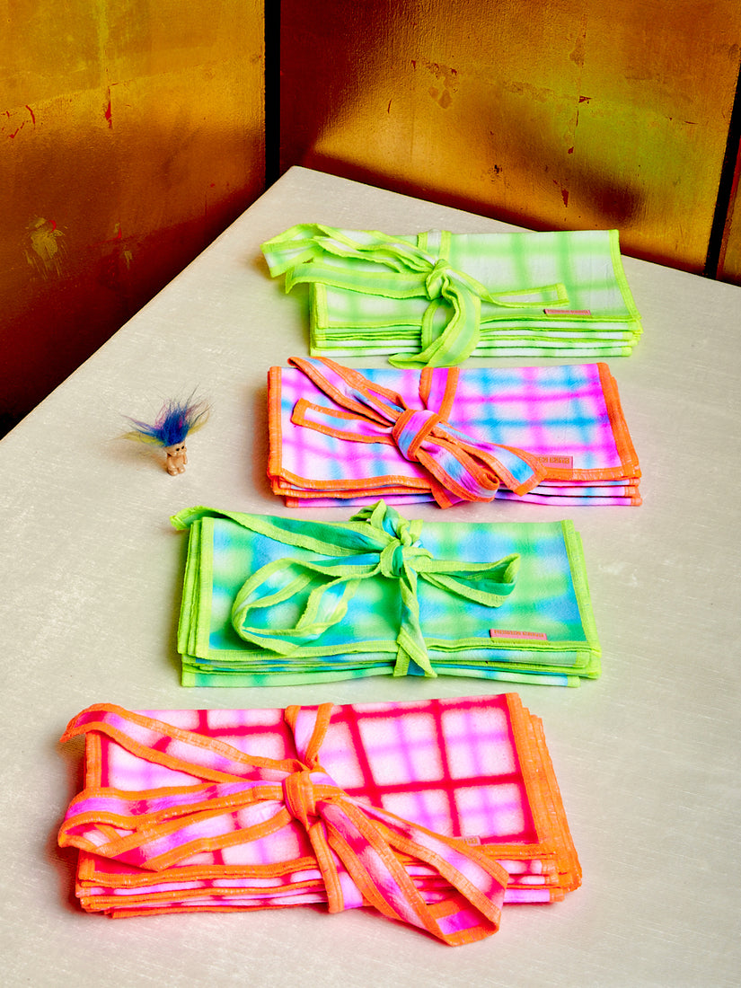 Four bundles of neon airbrushed napkins by Hotel Elma sit atop a surface. 