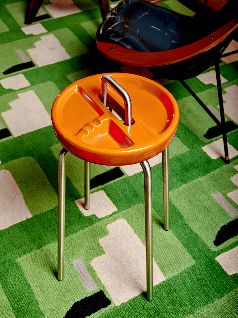 An orange Side Table Ashtray in a green carpeted living room.