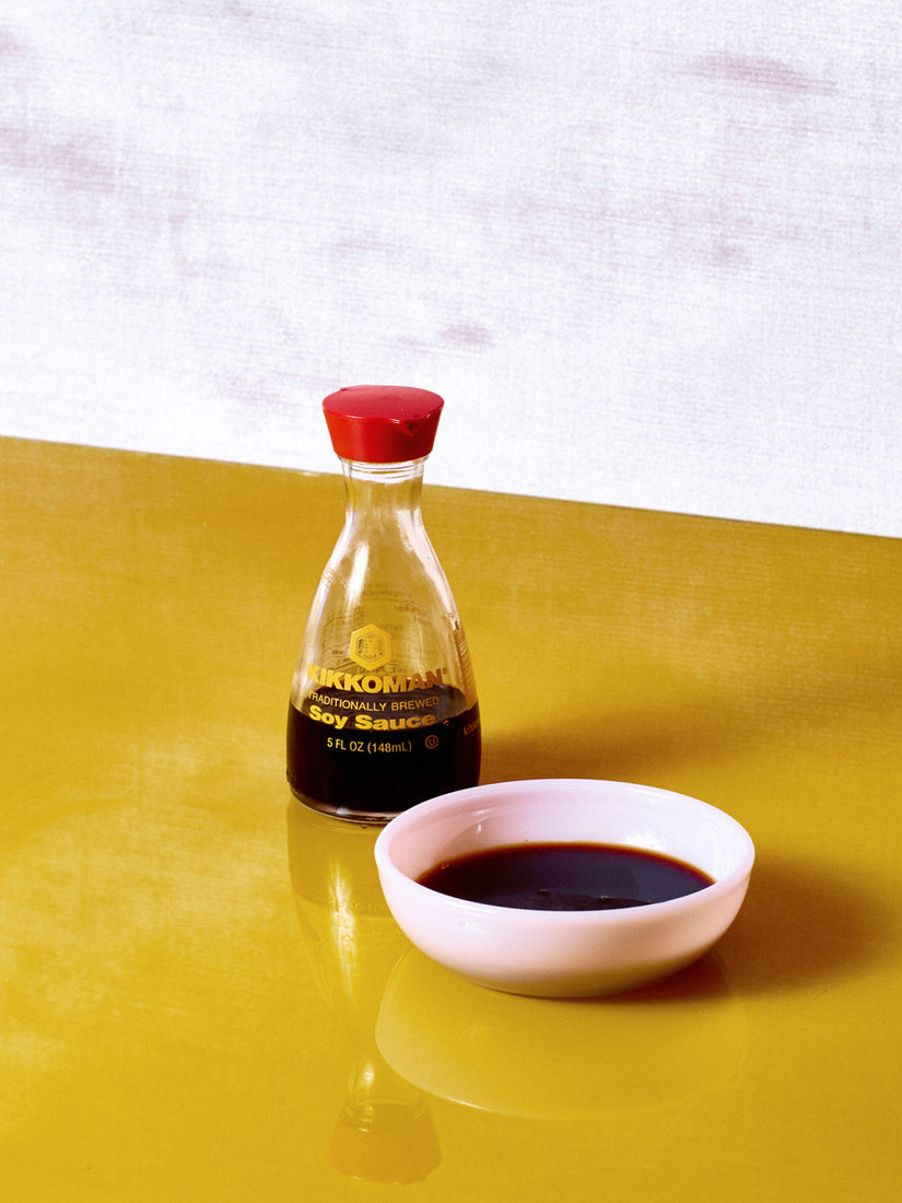 A kikkoman soy sauce bottle sits beside a small pink milk glass bowl full of soy sauce.