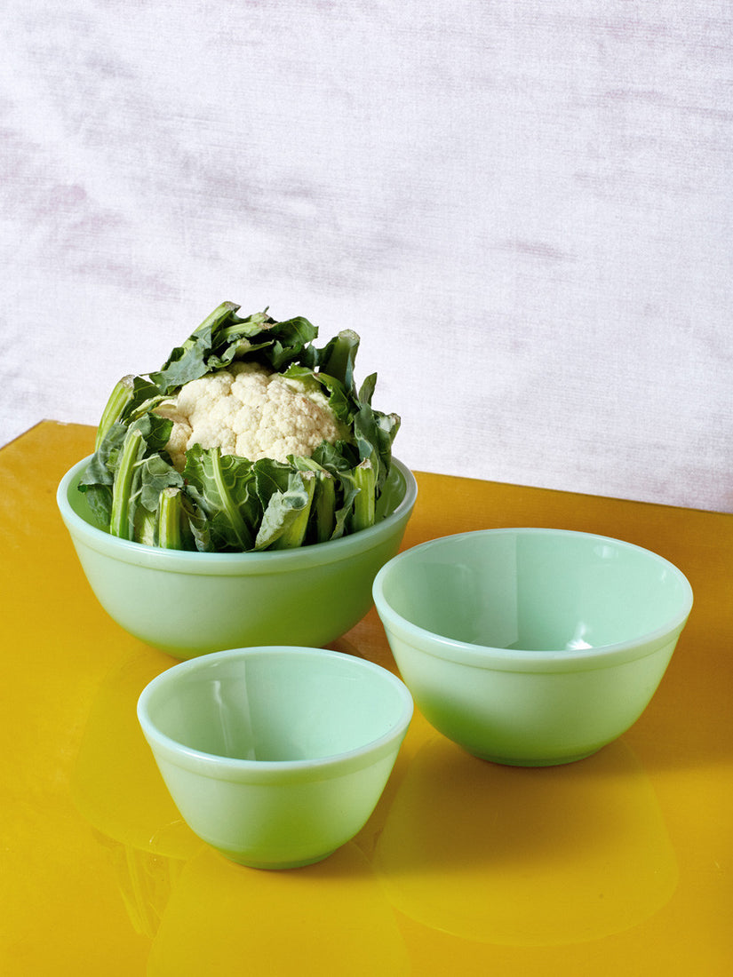 A large cauliflower sits inside the largest of 3 mixing bowls. The small and medium bowls sit in front of that.